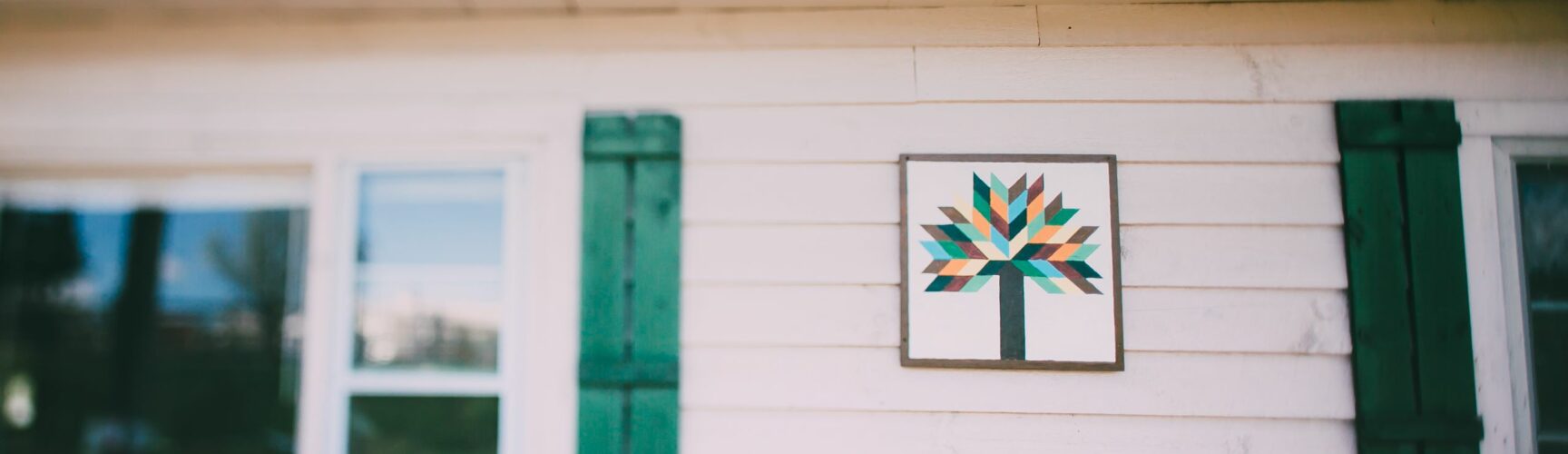 Barn quilt with tree decoration on white house
