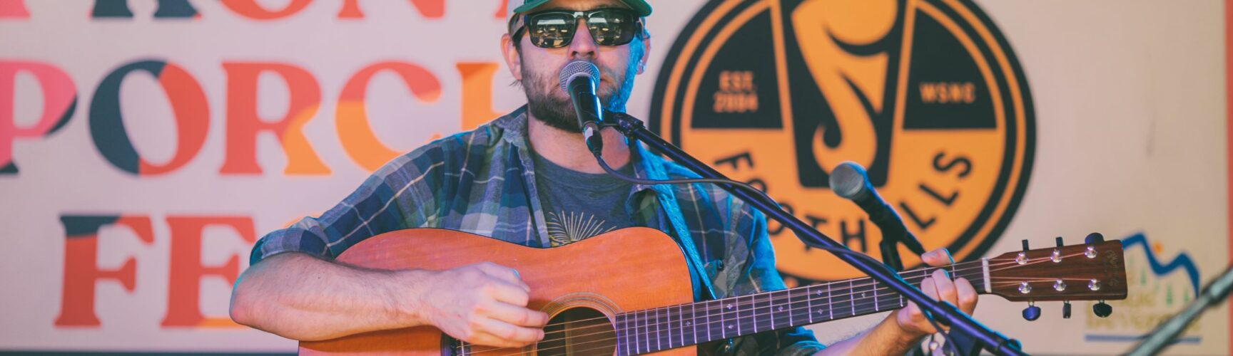 Man on stage with guitar, with Front Porch Fest sign in background